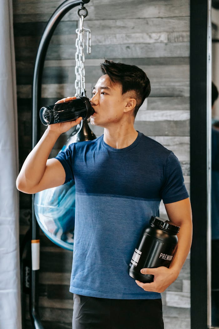 Asian athlete drinking water standing with bottle sports supplements